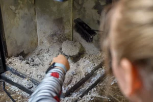 Une femme qui ramasse les cendres de bois depuis sa cheminée pour en faire une utilisation grace à des astuces de recyclage dans le jardin, pour le ménage, pour de l'anti odeur.. et éviter les déchets