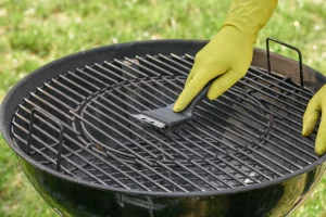 Un homme nettoye son barbecue et dégraisse la grille pour le rendre propre